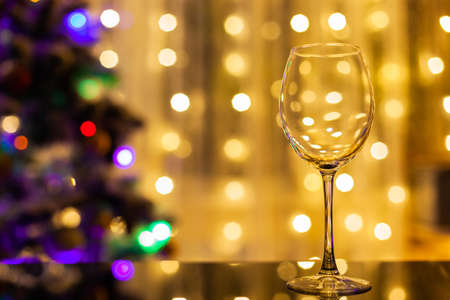 an empty wine glass stands on a black glass table against the background of the Christmas tree and...