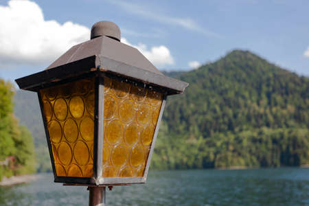 Street old vintage square-shaped lantern with brown glass against the backdrop of green mountains and blue sky with clouds, used as a background or textureの写真素材