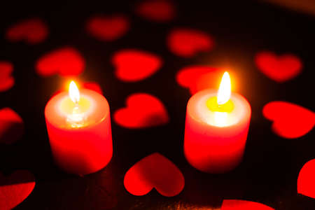 two red burning candles on a black textured background, around lie red heartsの写真素材