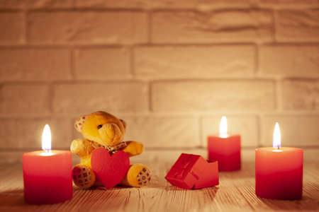 three red burning candles and a teddy bear with a red heart and a gift box against the white brick wall, use as a backdropの写真素材