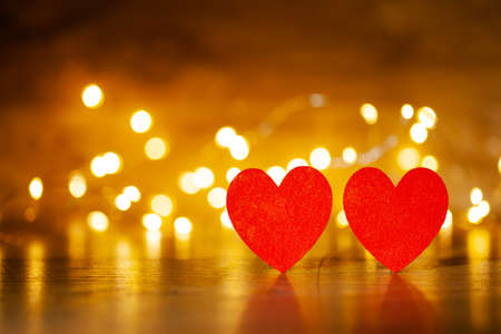 in the foreground are two krvs hearts, in the background on a wooden backdrop of a glowing garlandの写真素材