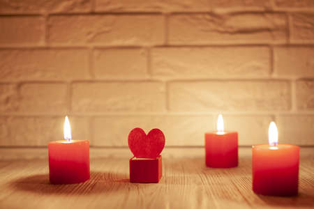 against the white brick wall three red burning candles and a box with a red heartの写真素材