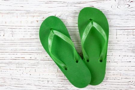 green rubber flip-flops on a white wooden background, view from aboveの写真素材