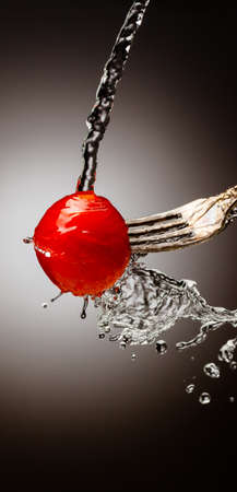 cherry tomatoes on a fork. vertical frame. Splashes of water. Place under the text. Black white background. gradientの写真素材