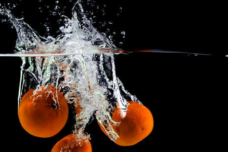three tangerines fall into the water on a black background, copy spaceの写真素材