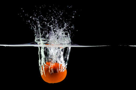 Mandarin falls into water creating spray on a black background, copy spaceの写真素材