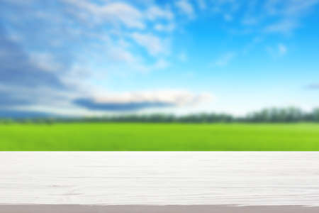 white wood table top on blur green field and blue sky with clouds background