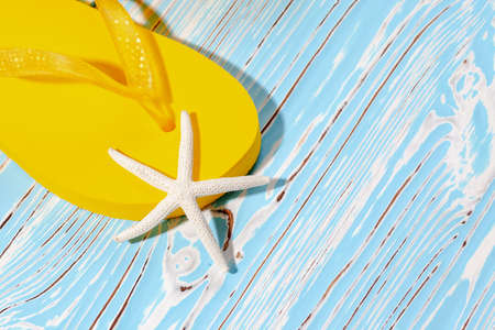 yellow rubber beach flip flops and starfish on a blue wooden background, place under the text