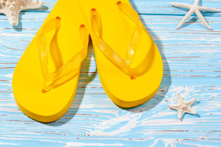 yellow rubber beach flip flops and starfish on a blue wooden background, place under the textの写真素材