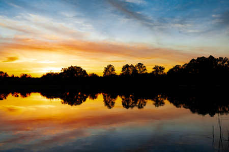 Sunset over the river, silhouette of the forest, mirror image in the water