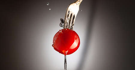 Cherry tomato ripe on a metal fork. A jet of water. Black white gradient backgroundの写真素材