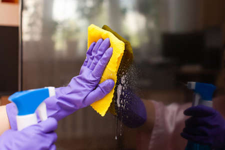 hand in a purple glove wipes the TV screen with a rag
