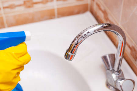 hand in a yellow rubber glove disinfects the water faucet in the bathroomの写真素材