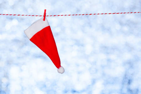 A small red Christmas cap hangs on a rope against a blurred shiny blue-gray background. Copy space. Blank for design, conceptの写真素材