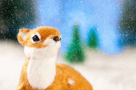 little toy deer sits in the snow. Around toy fir trees. New year greeting cardの写真素材