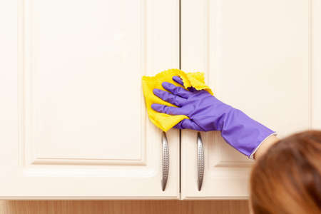 female hand in a purple rubber glove wipes the beige kitchen cabinet door. Yellow rag in handの写真素材