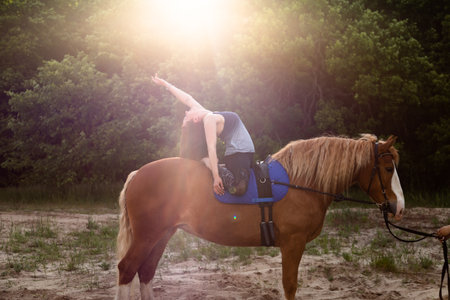 young woman doing yoga on a horse against the backdrop of treesの写真素材