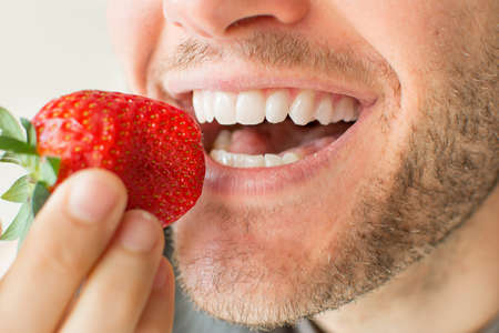 Young bearded man eating a strawberry