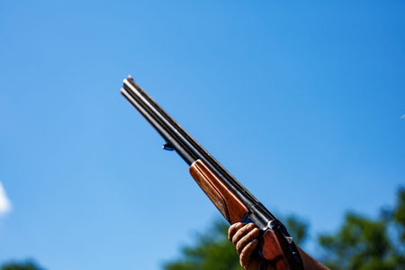 Hunting season. Close-up of a hunter's hand holding a gun against the blue sky.