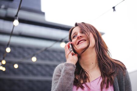 Beautiful young brunette woman in urban background talking on smartphoneの写真素材