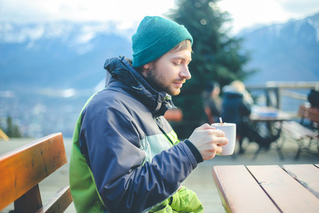 Man with cup of hot drink warms in winter mountains