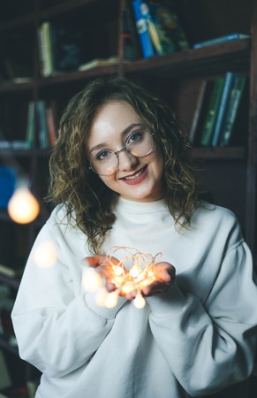 Portrait of young girl in glasses holding garlands of lightsの写真素材