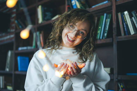 Portrait of young cute girl in glasses holding garlands of lightsの写真素材