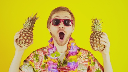 Happy lucky young man standing on yellow background with hawaiian shirt and two pineapplesの写真素材