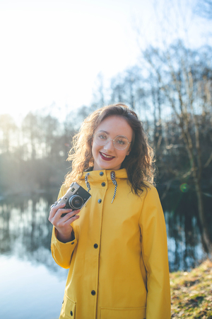 Vintage young hipster girl photographer in yellow jacket holding retro cameraの写真素材