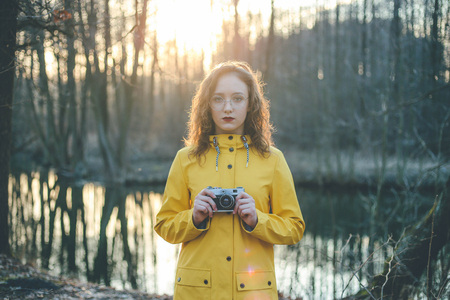 Portrait of teen hipster girl photographer in glasses with retro vintage camera at sunsetの写真素材