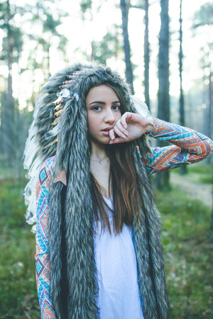 Portrait of young dramatic girl with Indian feather hat roach in forestの写真素材