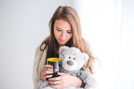 Portrait of the beautiful young woman with teddy bear plush and cup of coffee in bedroomの写真素材