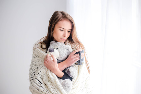 Young beautiful woman holding teddy bear plush and cup of coffee in bedroomの写真素材