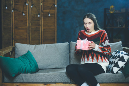 Shocked young woman holding decorative christmas gift box, copy space for textの写真素材