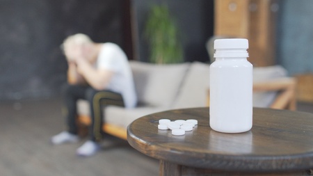 Sad young man with headache sitting on sofa at home with a pills on the tableの写真素材