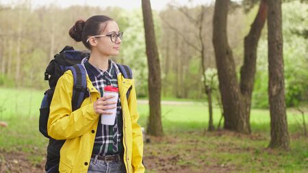 Young tourist woman holding bottle of hot drink, copy space. Travel and hiking concept