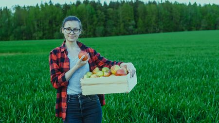 Portrait of young smiling woman farmer holding wooden box of freshly fruits - apples and pearsの写真素材