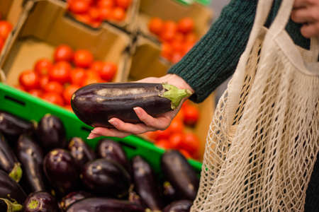 Woman choosing eggplant in the supermarket. Close up of hand holding eggplant in farm market.の写真素材