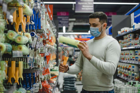 A buyer wearing medical mask chooses a paint roller in a hardware store.の写真素材