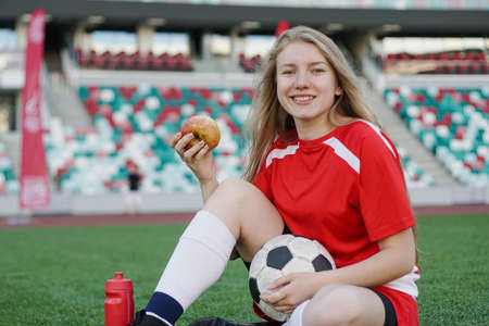 Portrait of young female football player sitting on soccer field with apple after the trainingの写真素材