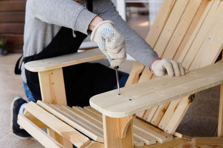 Professional carpenter assembling wooden adirondack chair with screwdriver. Manual work and do-it-yourselfの写真素材