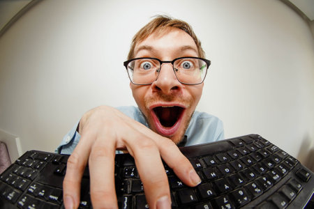 Fisheye portrait of crazy nerd with glasses typing keyboard, looking at cameraの写真素材