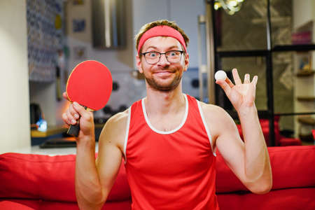 Funny crazy athlete nerd with ping pong table tennis racket and ball at home.の写真素材