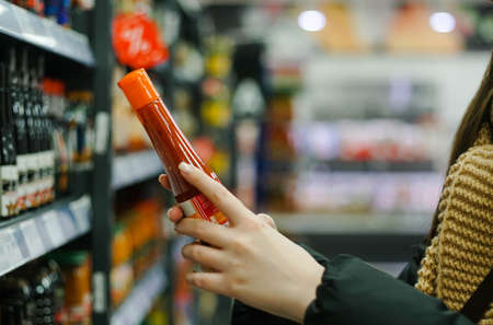 Female hand choosing natural red chili pepper sauce at store.の写真素材