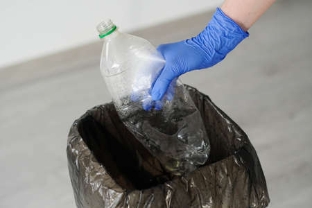 Woman Wearing Rubber Gloves Throwing Empty Plastic Bottle to The Trash Can.の写真素材