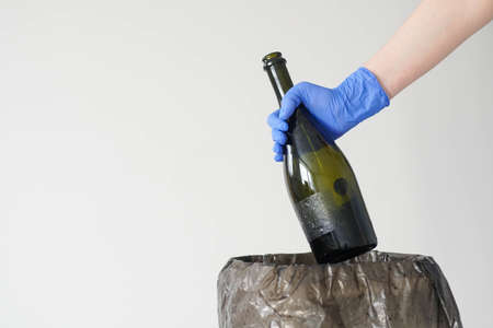 Woman In Gloves Throwing Empty Glass Bottle To The Trash Can. Close up.