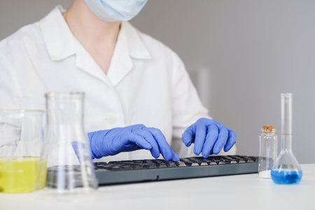 Woman scientist in gloves working on the keyboard at desktop in laboratory.の写真素材