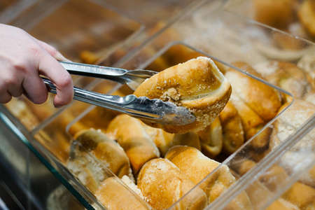 Close up of woman takes fresh baked bun with tongs at a bakery store.の写真素材