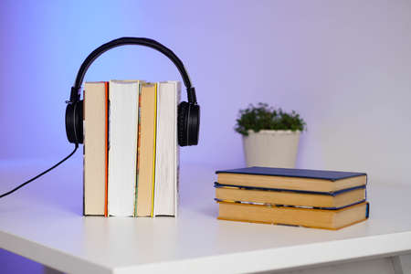 Black headphones with stack of books on blue background. Audio books or education concept.の写真素材