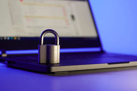 Locked metal padlock on a laptop keyboard over blue background. Cyber security, antivirus software concept.の写真素材